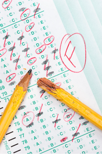 Close-up of a graded school test with incorrect answers marked in red, including a large circled failing grade, and broken pencils resting on the paper.